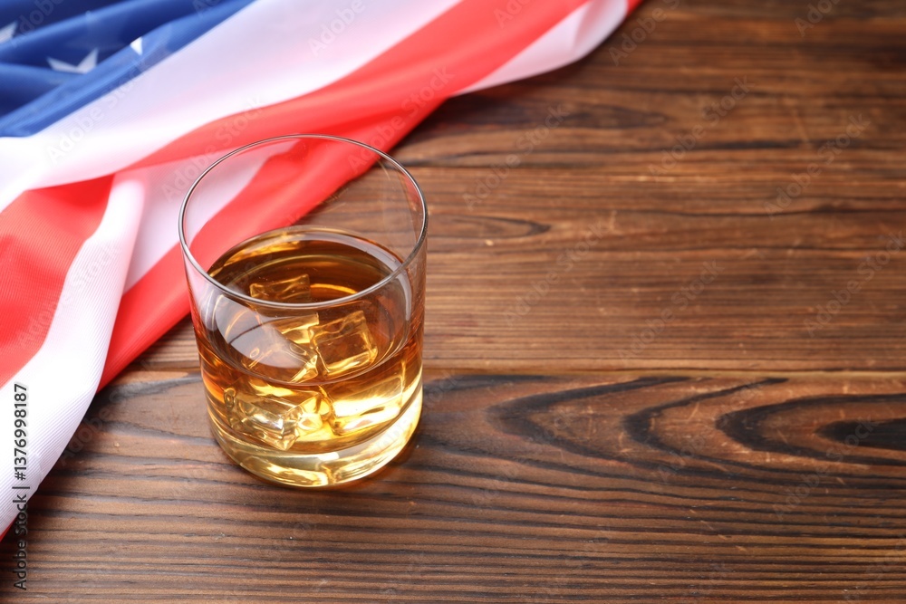 Glass of whiskey and American flag on wooden table. Space for text