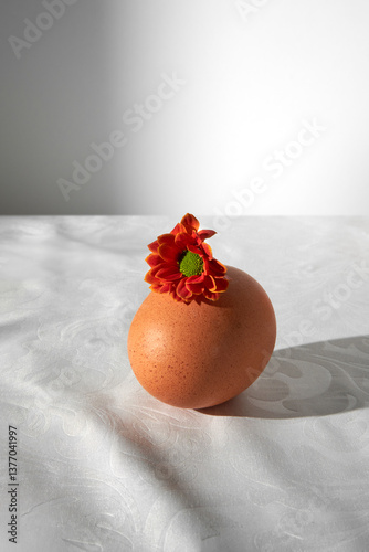 Brown egg with small flower on white tablecloth.  photo