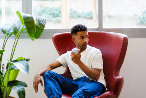 Pensive man in modern armchair drinking tea. Hygge