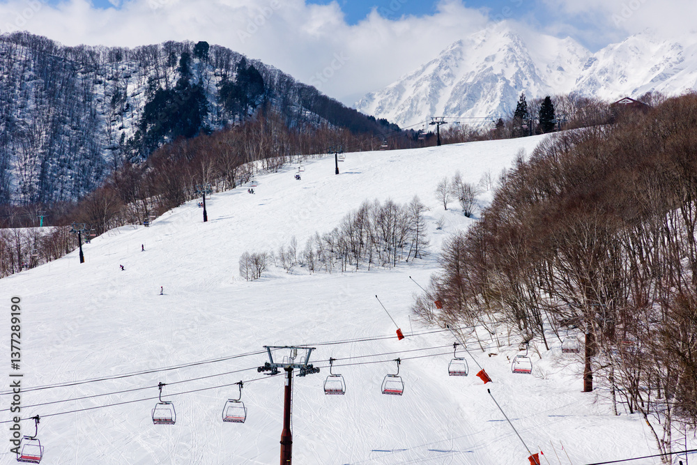 Empty ski chairlift with large, wide slope and mountains behind on a sunny day