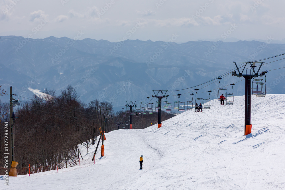 Snowboarders on a ski lift near the top of mountain with slope below at Tsugaike, Hakuba, Japan