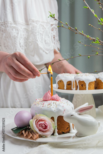 A woman in a white dress lights a candle on an Easter cake.
