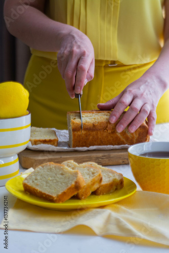 Woman in yellow clothes cutting lemon cake.