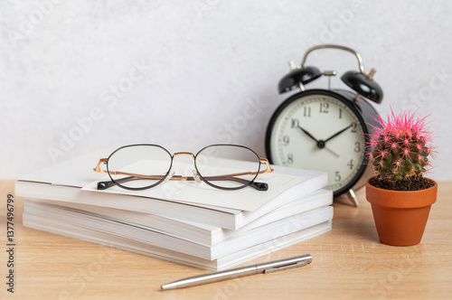 Obraz na płótnie Eyeglasses resting on stack of notebooks with pen, alarm clock, and cactus w salonie