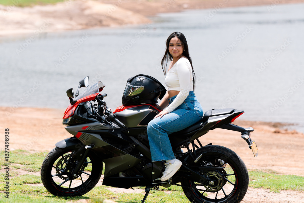 Obraz premium Young woman relaxing on her sport motorcycle by a serene lake, embracing the thrill of adventure and the essence of freedom