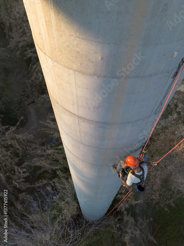 Rope access technician performing inspection on concrete chimney using drone view