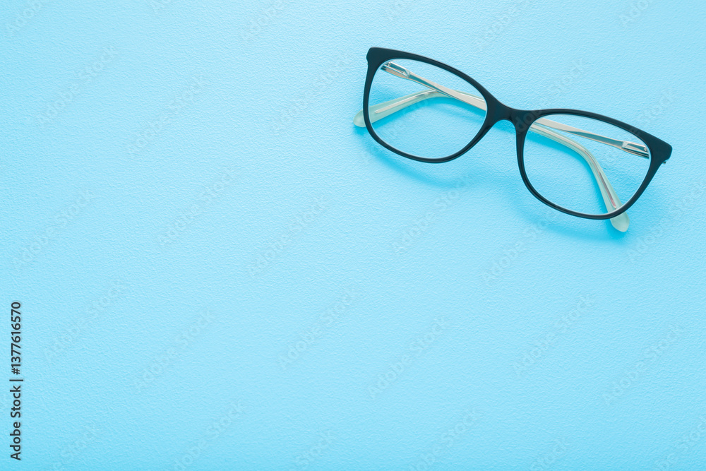 Eyeglasses with dark black plastic frame on light blue table background. Pastel color. Closeup. Empty place for text. Top down view.