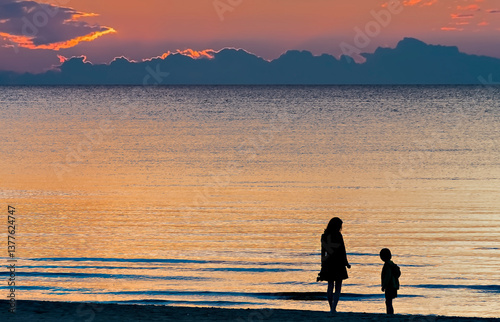 Silhouettes of family walking on sandy beach of the Baltic Sea at sunset