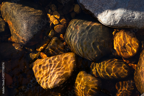 Abstract warm light and water patterns textures on stones in shallow water