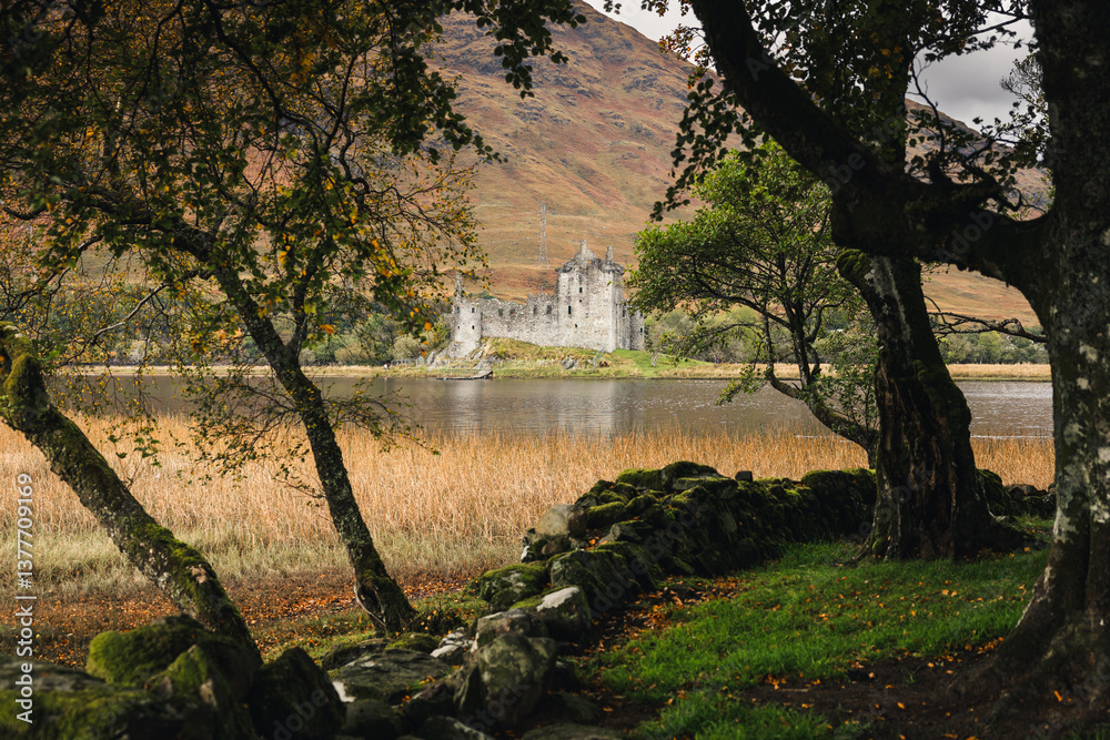 Rolling hills and grazing sheep frame Kilchurn Castle, its ancient ruins reflecting in Loch Awe. A timeless Highland scene bathed in golden Scottish light.