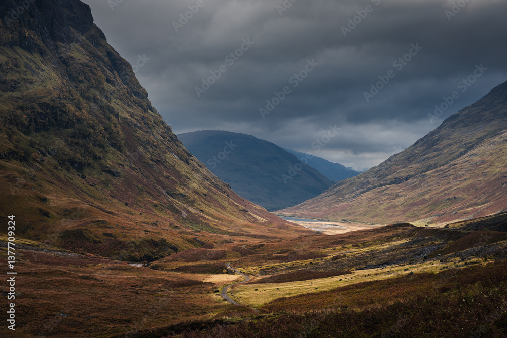 Dramatic peaks and misty valleys define Glen Coe, Scotland’s iconic Highland landscape. Golden light dances on rugged slopes, creating a scene of wild, untamed beauty.