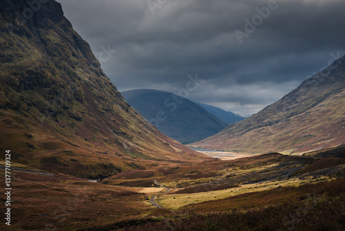 Obraz na płótnie Dramatic peaks and misty valleys define Glen Coe, Scotland’s iconic Highland landscape. Golden light dances on rugged slopes, creating a scene of wild, untamed beauty. w salonie