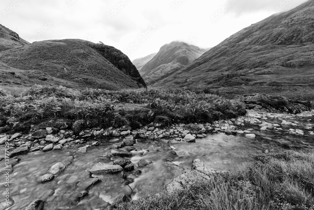 Dramatic peaks and misty valleys define Glen Coe, Scotland’s iconic Highland landscape. Golden light dances on rugged slopes, creating a scene of wild, untamed beauty.