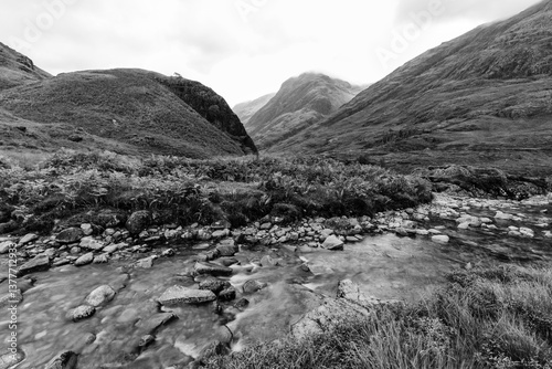 Obraz na płótnie Dramatic peaks and misty valleys define Glen Coe, Scotland’s iconic Highland landscape. Golden light dances on rugged slopes, creating a scene of wild, untamed beauty. w salonie