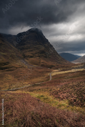 Dramatic peaks and misty valleys define Glen Coe, Scotland’s iconic Highland landscape. Golden light dances on rugged slopes, creating a scene of wild, untamed beauty.