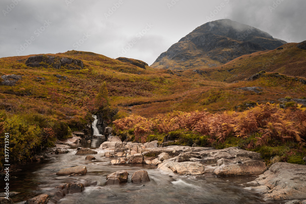 Dramatic peaks and misty valleys define Glen Coe, Scotland’s iconic Highland landscape. Golden light dances on rugged slopes, creating a scene of wild, untamed beauty.