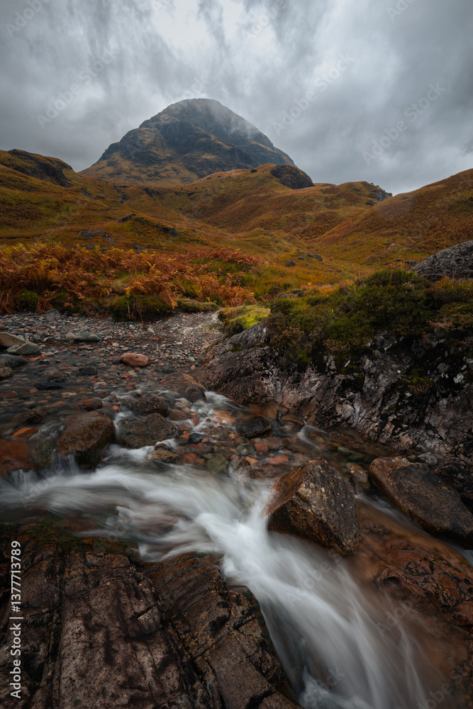 Dramatic peaks and misty valleys define Glen Coe, Scotland’s iconic Highland landscape. Golden light dances on rugged slopes, creating a scene of wild, untamed beauty.