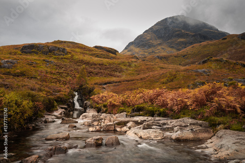 Obraz na płótnie Dramatic peaks and misty valleys define Glen Coe, Scotland’s iconic Highland landscape. Golden light dances on rugged slopes, creating a scene of wild, untamed beauty. w salonie