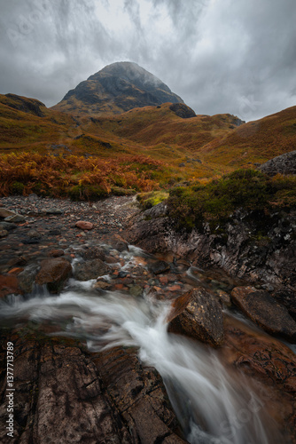 Obraz na płótnie Dramatic peaks and misty valleys define Glen Coe, Scotland’s iconic Highland landscape. Golden light dances on rugged slopes, creating a scene of wild, untamed beauty. w salonie