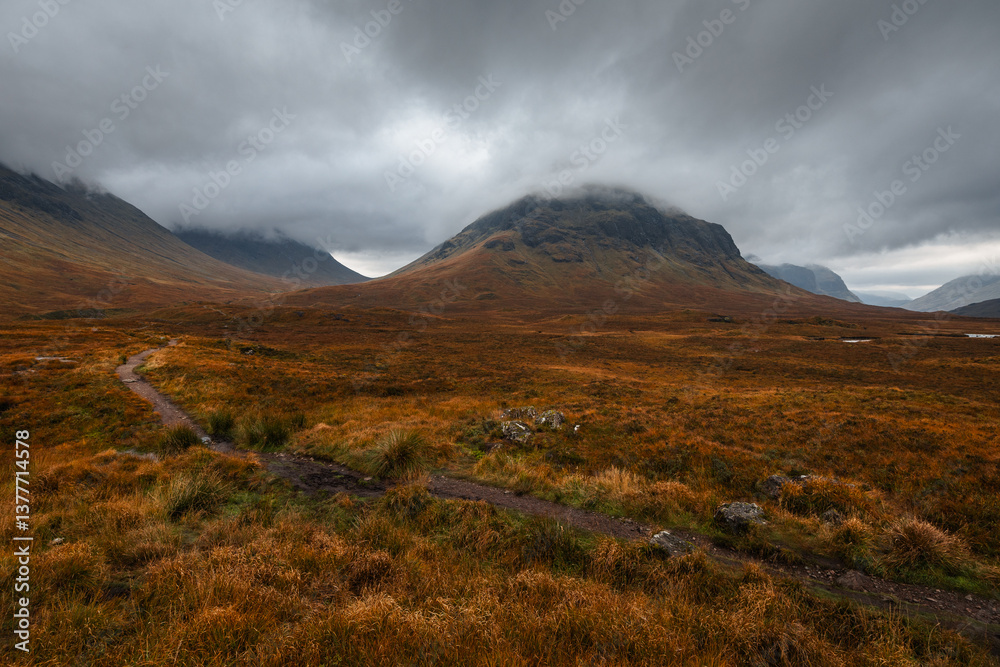 Dramatic peaks and misty valleys define Glen Coe, Scotland’s iconic Highland landscape. Golden light dances on rugged slopes, creating a scene of wild, untamed beauty.