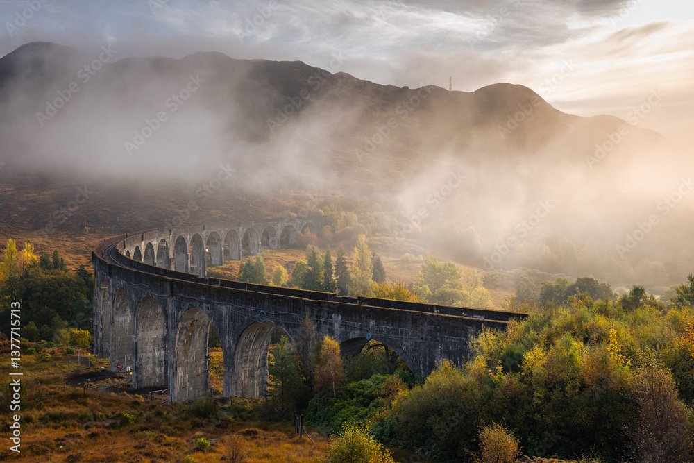 The morning train steams across the Glenfinnan Viaduct, its plume rising against the Highland mist. Golden light touches the hills, creating a scene of timeless beauty in Scotland’s heart.