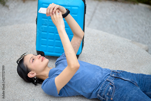 Tourist resting flat on stone surface using phone beside suitcase