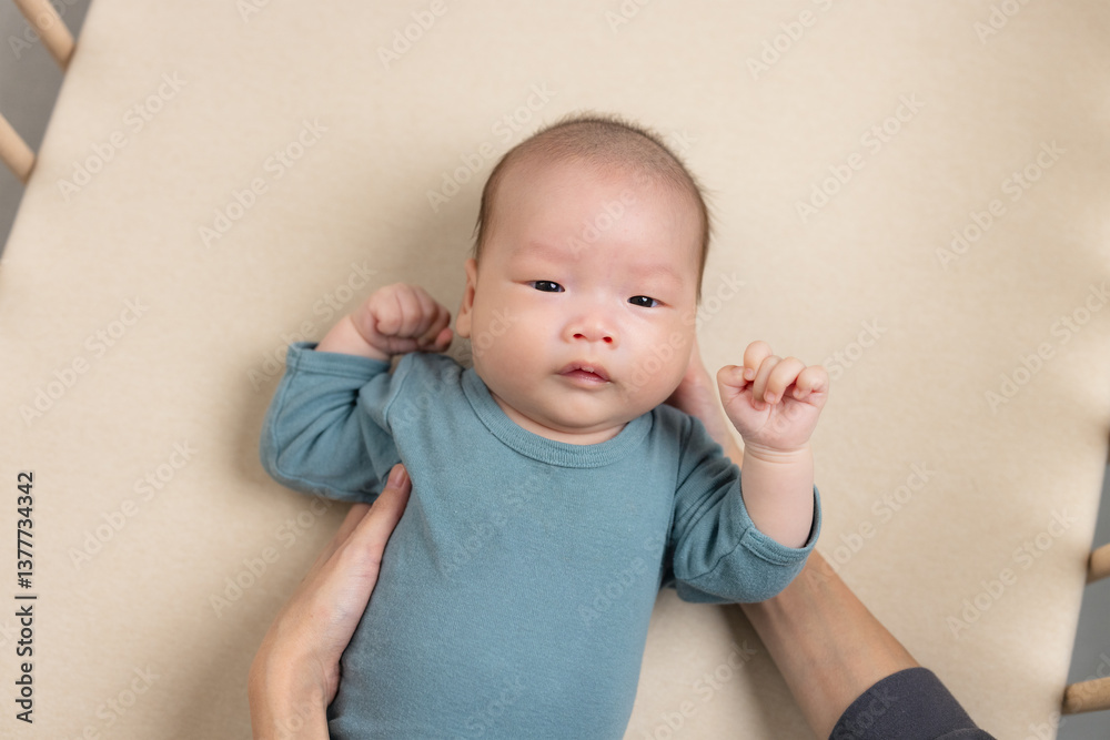 Cute baby lying on soft beige mattress with hands raised