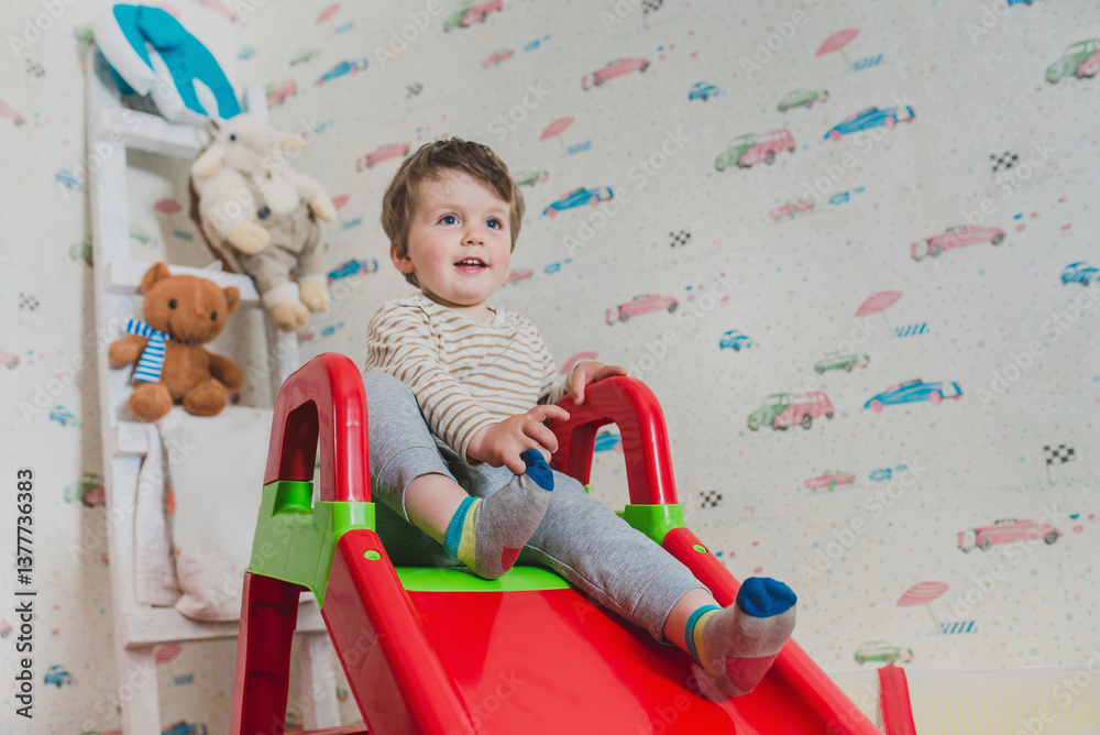 Fototapeta premium Baby slides down a slide, games in the nursery. Carefree childhood, children's centers and attractions. Choosing a nanny, safe leisure for children