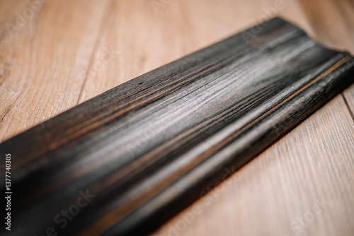 Close-up of a dark wooden molding plank with a weathered texture, placed diagonally on a light wood surface for contrast and detail..