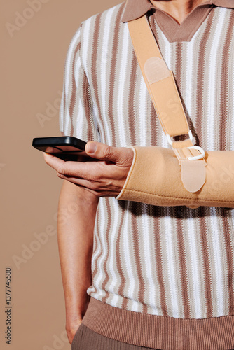 Man with tennis elbow wearing arm sling using smartphone