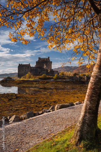 Obraz na płótnie Eilean Donan Castle stands majestically amid autumn hues, its reflection shimmering in calm waters. Misty Highlands and golden trees create a scene of timeless beauty. w salonie