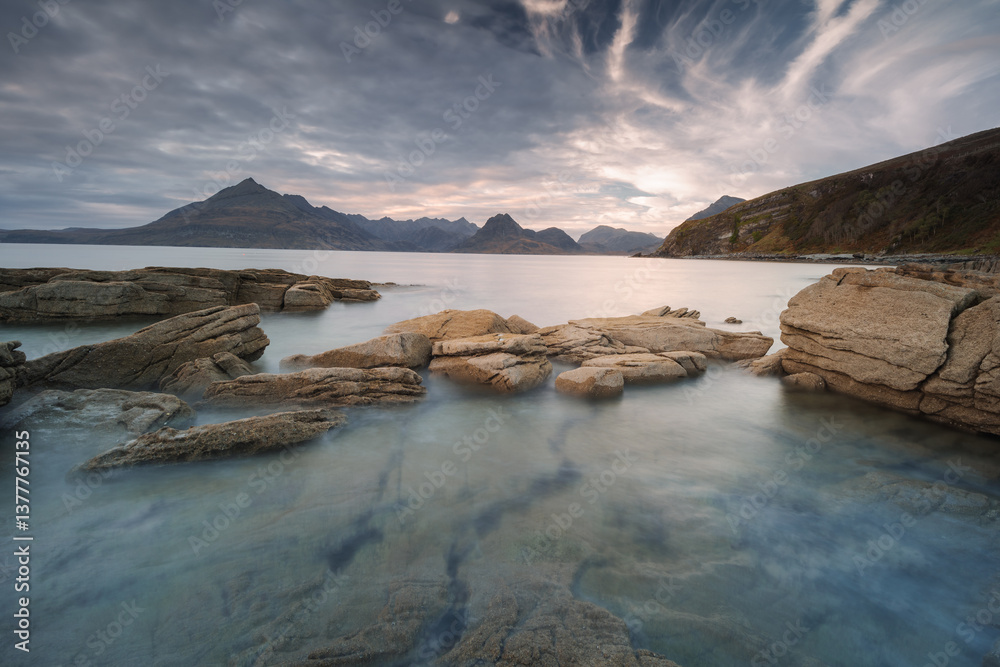 Dramatic waves crash against Elgol’s rugged coast, with the Cuillin Mountains rising in the misty distance. Autumn’s golden light enhances this wild, untamed beauty.