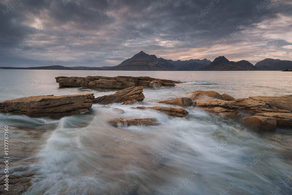 Dramatic waves crash against Elgol’s rugged coast, with the Cuillin Mountains rising in the misty distance. Autumn’s golden light enhances this wild, untamed beauty.