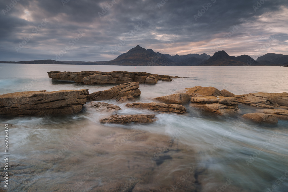 Dramatic waves crash against Elgol’s rugged coast, with the Cuillin Mountains rising in the misty distance. Autumn’s golden light enhances this wild, untamed beauty.