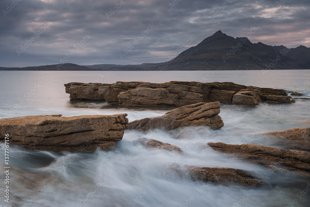Dramatic waves crash against Elgol’s rugged coast, with the Cuillin Mountains rising in the misty distance. Autumn’s golden light enhances this wild, untamed beauty.