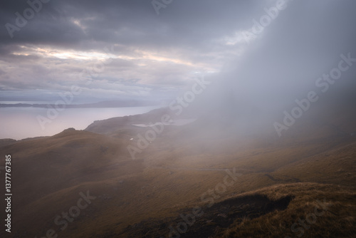 The Old Man of Storr emerges from autumn mist, its towering pinnacles glowing in golden morning light. A mystical, otherworldly Highland scene.