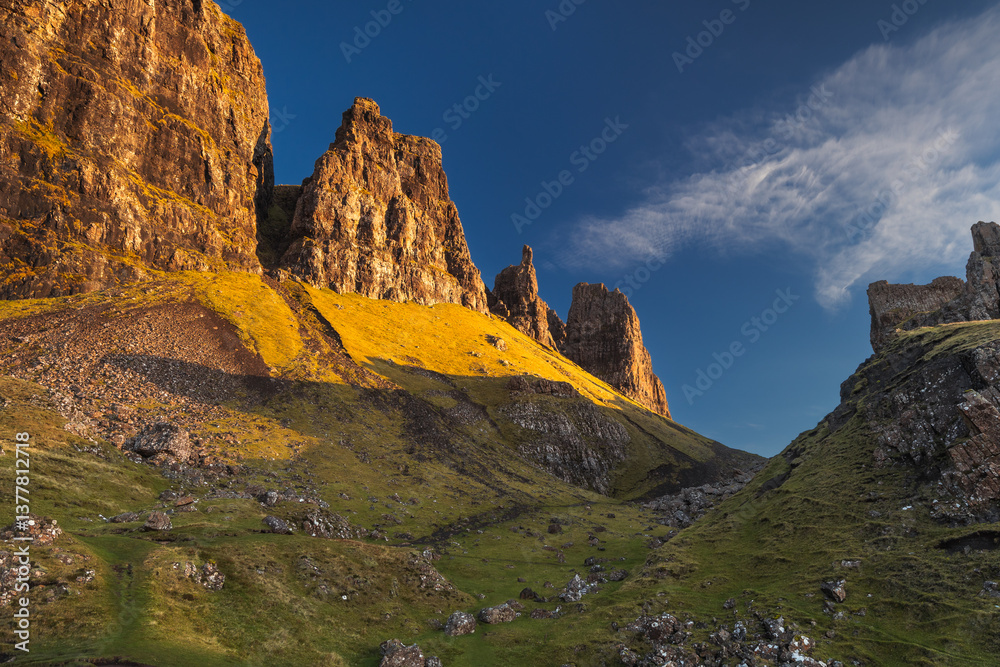 Autumn light bathes the Quiraing on Skye, casting long shadows over its dramatic cliffs and rolling hills. The landscape glows with golden hues, a breathtaking Highland scene.
