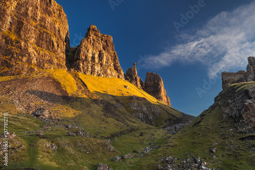 Obraz na płótnie Autumn light bathes the Quiraing on Skye, casting long shadows over its dramatic cliffs and rolling hills. The landscape glows with golden hues, a breathtaking Highland scene. w salonie