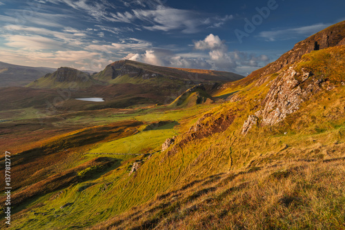 Obraz na płótnie Autumn light bathes the Quiraing on Skye, casting long shadows over its dramatic cliffs and rolling hills. The landscape glows with golden hues, a breathtaking Highland scene. w salonie
