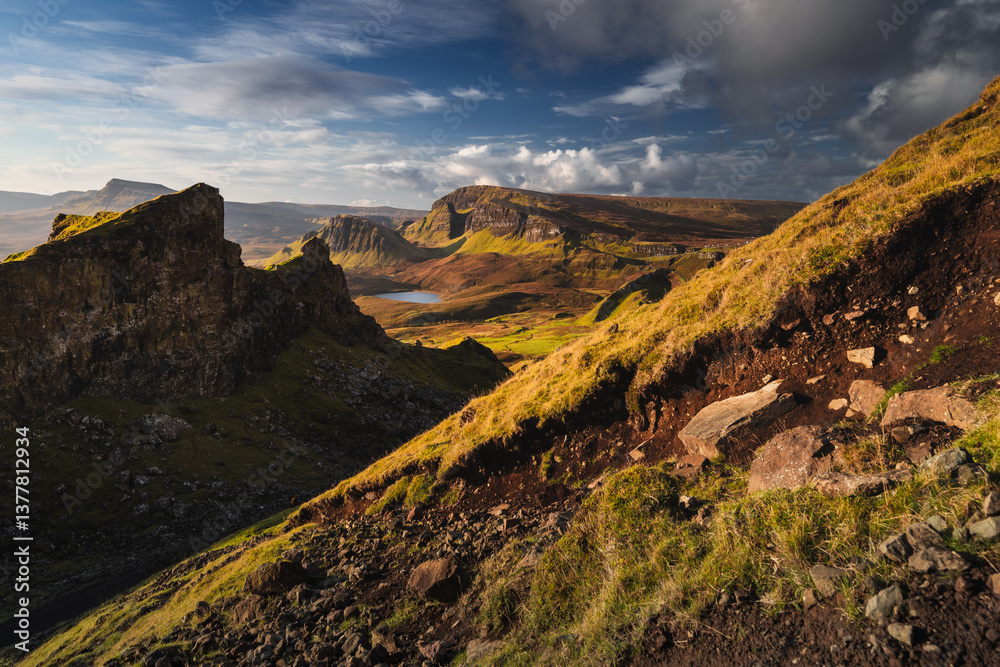 Autumn light bathes the Quiraing on Skye, casting long shadows over its dramatic cliffs and rolling hills. The landscape glows with golden hues, a breathtaking Highland scene.