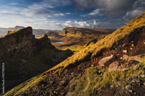 Obraz na płótnie Autumn light bathes the Quiraing on Skye, casting long shadows over its dramatic cliffs and rolling hills. The landscape glows with golden hues, a breathtaking Highland scene. w salonie