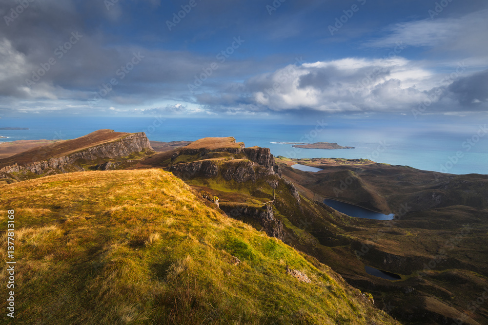Autumn light bathes the Quiraing on Skye, casting long shadows over its dramatic cliffs and rolling hills. The landscape glows with golden hues, a breathtaking Highland scene.