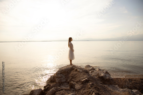 Young woman standing on a rock with white dress, dreamy in front of the sea