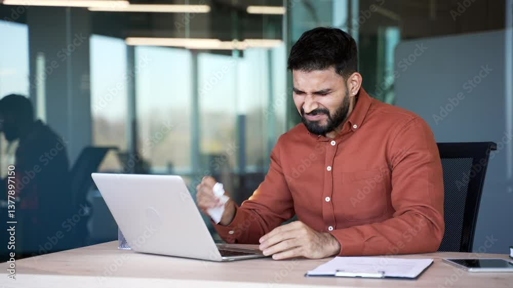 Allergic businessman sneezes and wipes his nose with a handkerchief while sitting at the desk at the workplace in a modern business office. Sick handsome entrepreneur suffering from seasonal allergies Allergic businessman sneezes and wipes his nose with a handkerchief while sitting at the desk at the workplace in a modern business office. Sick handsome entrepreneur suffering from seasonal allergies