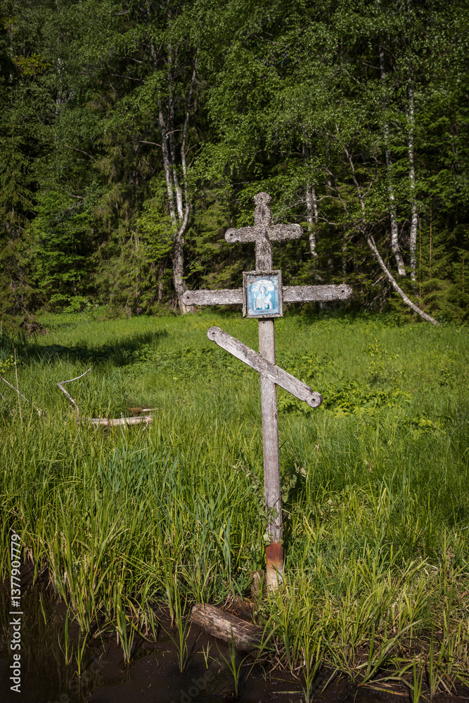 Old wooden cross in a wetland. A worship cross with an icon at the site of a holy spring in the forest. Cross covered with lichen. Consecrated spring in a forest area.