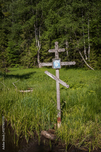 Old wooden cross in a wetland. A worship cross with an icon at the site of a holy spring in the forest. Cross covered with lichen. Consecrated spring in a forest area.