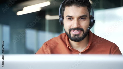 Smiling male corporate operator in headset working in customer support service on helpline telesale talking using laptop in business office. The agent of the call center advises the client. Close up