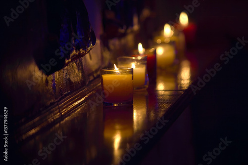 several decorative candles burning in clear glasses on a shelf in the dark