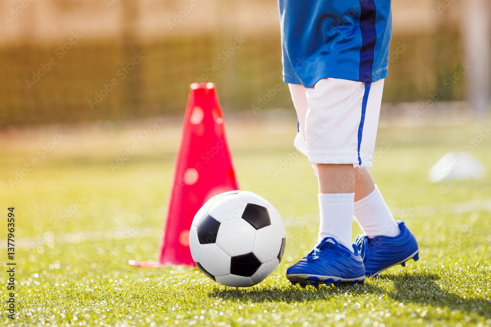 Obraz premium Legs of Little Child with Soccer Ball. Soccer Ball and Pylons on Grass. Youth Soccer Player Training. Young Footballer with Ball Training with Cones