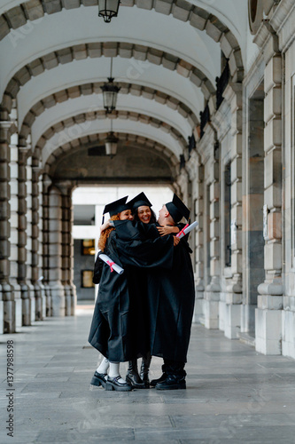Obraz na płótnie Group of graduated students wearing gowns and holding diplomas are hugging under university archway w salonie